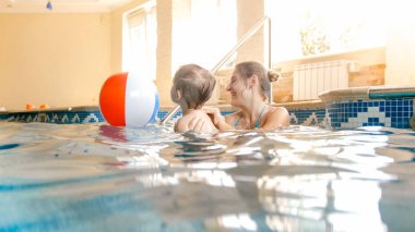 Yaz otel tatil yüzme havuzunda renkli şişme plaj topu ile oynayan genç anne ile mutlu gülen bebek çocuk portresi