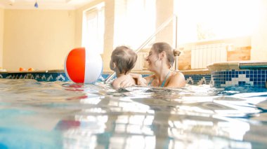 Genç anne onun küçük 3 yaşındaki çocuk yüzme ve kapalı yüzme havuzunda renkli plaj topu ile oynarken öğretim Görüntü
