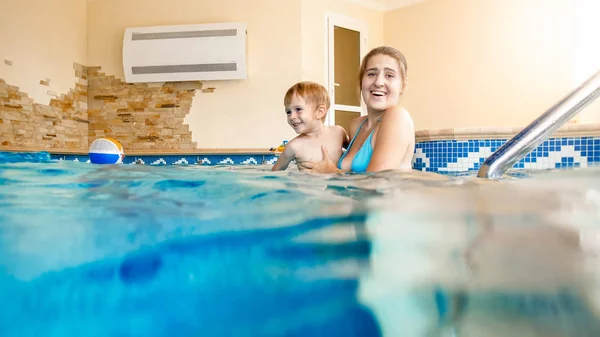 Porträt eines fröhlichen, jungen Motten mit einem dreijährigen Kleinkind, das im Pool des Hauses spielt. Kind lernt Schwimmen mit Eltern. Familie hat Spaß im Sommer — Stockfoto