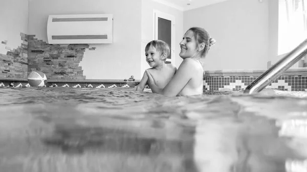 Ritratto in bianco e nero di felice giovane madre con piccolo bambino che nuota nella piscina coperta in palestra — Foto Stock