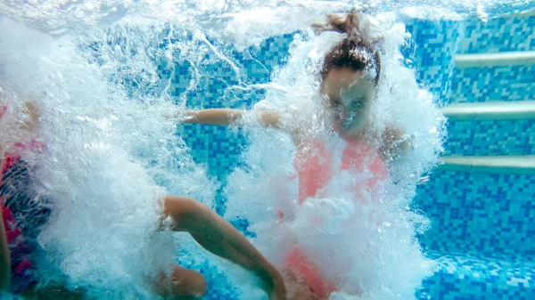 Underwater image of two teenage girls jumping in swimming pool at summer hotel resort — Stock Photo, Image