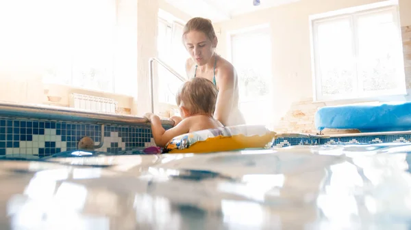 Portrait of 3 years old toddler boy with young mother swimming in the indoors pool. Child learning swimming and doing sports. Family enjoying and having fun in water — Stock Photo, Image