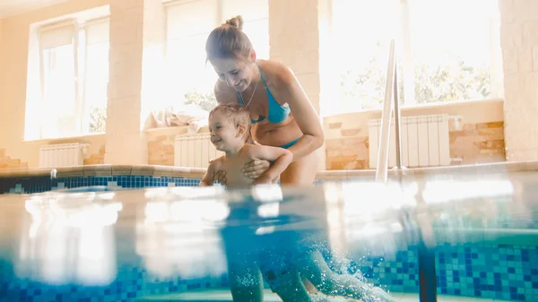 Porträt einer glücklich lächelnden Mutter mit ihrem 3-jährigen kleinen Sohn, der im Pool der Turnhalle schwimmt. Familie rastaxen, Spaß haben und im Wasser spielen — Stockfoto