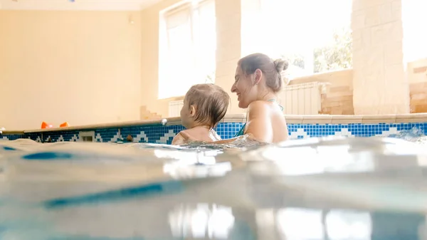 Porträt eines fröhlichen, jungen Motten mit einem dreijährigen Kleinkind, das im Pool des Hauses spielt. Kind lernt Schwimmen mit Eltern. Familie hat Spaß im Sommer — Stockfoto