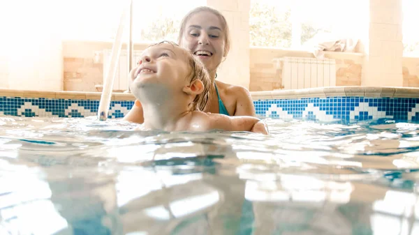 Ritratto di bambino sorridente felice che impara a nuotare con la madre in piscina. Famiglia divertendosi e rilassandosi in piscina — Foto Stock