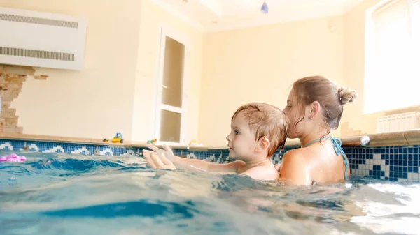 Bild der jungen Mutter, die ihrem kleinen 3-jährigen Kind das Schwimmen beibringt und im Hallenbad mit bunten Strandbällen spielt — Stockfoto