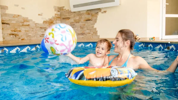 Porträt eines fröhlich lachenden Kleinkindes mit junger Mutter beim Spielen mit buntem aufblasbarem Strandball im Schwimmbad des Sommerhotel-Resorts — Stockfoto