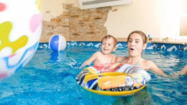 Bild der jungen Mutter, die ihrem kleinen 3-jährigen Kind das Schwimmen beibringt und im Hallenbad mit bunten Strandbällen spielt — Stockfoto