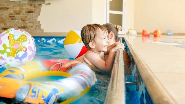 Bild der jungen Mutter, die ihrem kleinen 3-jährigen Kind das Schwimmen beibringt und im Hallenbad mit bunten Strandbällen spielt — Stockfoto