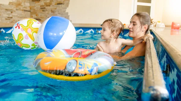 Porträt eines fröhlich lachenden Kleinkindes mit junger Mutter beim Spielen mit buntem aufblasbarem Strandball im Schwimmbad des Sommerhotel-Resorts — Stockfoto