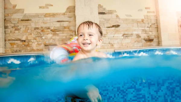 Oyuncaklarla oynayan ve kapalı yüzme havuzunda yüzmeyi öğrenen mutlu gülen ve gülümseyen küçük çocuğun fotoğrafı — Stok fotoğraf