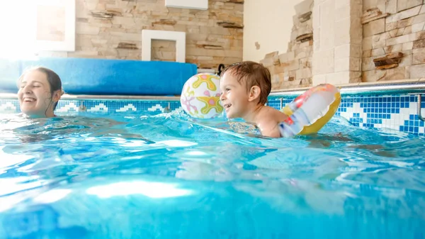 Porträt eines fröhlich lächelnden Kleinkindes, das mit Mutter im Innenpool mit aufblasbarem bunten Strandball spielt — Stockfoto