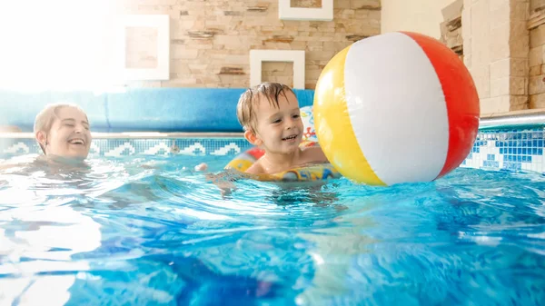 Retrato de niño riendo feliz con madre joven jugando con la bola inflable colorida de la playa en la piscina en el complejo del hotel del verano —  Fotos de Stock
