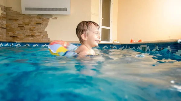 Porträt eines fröhlichen Kleinkindes, das mit aufblasbarem Beachball und buntem Ring im Hallenbad im Haus spielt — Stockfoto