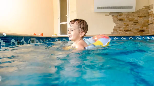 Foto av glad skratt och leende liten pojke leker med leksaker och lärande simning i inomhusbassäng — Stockfoto