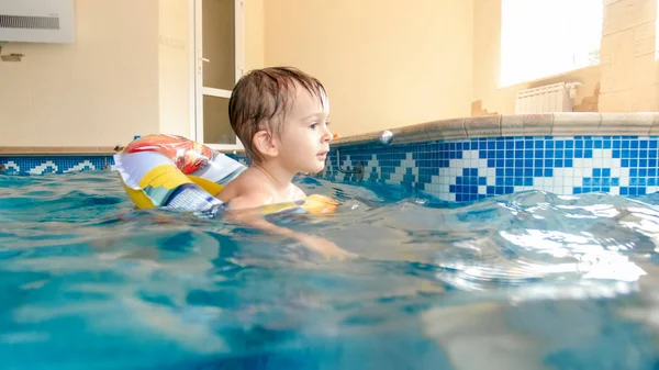 Porträt eines lachenden und lächelnden 3-jährigen Jungen, der mit aufblasbarem bunten Ring schwimmt und mit Beachball im Schwimmbad spielt — Stockfoto