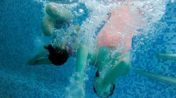 Imagen submarina de dos adolescentes saltando y buceando en la piscina en el gimnasio —  Fotos de Stock