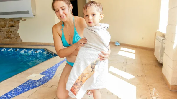 Porträt einer schönen lächelnden jungen Frau, die ihren 3-jährigen kleinen Sohn nach dem Schwimmen im Hallenbad bedeckt und abwischt — Stockfoto