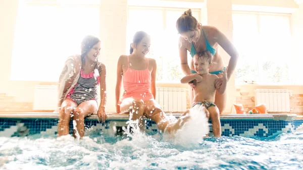 Retrato de família alegre feliz sentado à beira da piscina e salpicando água com os pés. Família brincando e se divertindo na piscina — Fotografia de Stock