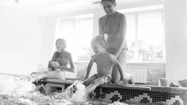 Foto einer fröhlich lachenden Familie mit Kindern, die im Hallenbad mit Füßen Wasser planschen. Familie spielt und hat Spaß am Schwimmbad — Stockfoto