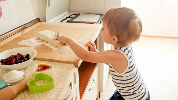 Foto di 3 anni bambino bambino rotolamento pasta su tavola di legno e biscotti da forno per la prima colazione. Bambino che cucina in cucina. Bambini intelligenti — Foto Stock