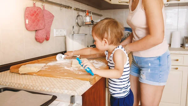 Porträtt av ung vacker kvinna undervisning hennes lilla barn pojke att göra kakor och bakning pajer på kök hemma — Stockfoto