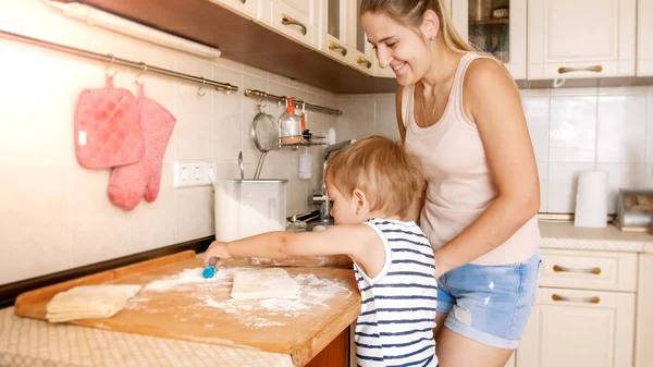 Ritratto di bambino sorridente felice con giovane madre che cucina e cuoce in cucina. Insegnamento dei genitori ed educazione dei bambini a casa — Foto Stock