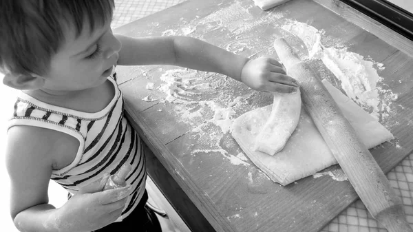 Черно-белый портрет восхитительного 3-летнего мальчика, который готовит на кухне. Детское питание и выпечка на кухне на завтрак — стоковое фото