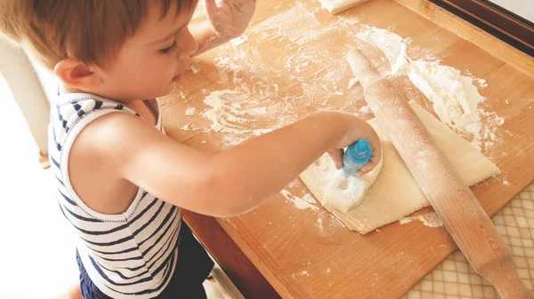 Крупный план портрета очаровательного 3-летнего малыша, пекущего печенье и катящегося теста с деревянной шпилькой. Маленький повар — стоковое фото