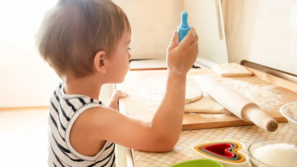 Foto di 3 anni bambino bambino rotolamento pasta su tavola di legno e biscotti da forno per la prima colazione. Bambino che cucina in cucina. Bambini intelligenti — Foto Stock