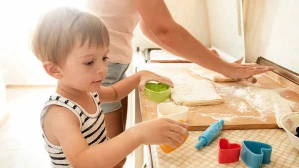 彼女の3歳の幼児の男の子を教える若い笑顔の母親の肖像画は、キッチンでクッキーを作ります — ストック写真