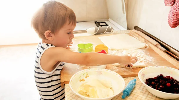 Primo piano ritratto di adorabile bambino di 3 anni ragazzo rotolamento pasta di grano con mattarello e biscotti di taglio con speciale figurato taglierina di plastica. Chuld cottura e cottura in cucina — Foto Stock