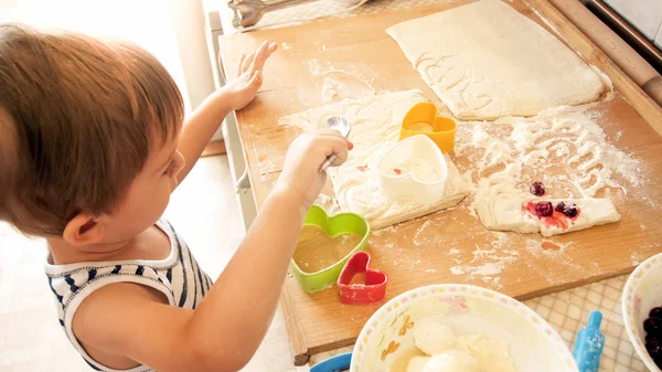 Primo piano ritratto di adorabile bambino di 3 anni ragazzo rotolamento pasta di grano con mattarello e biscotti di taglio con speciale figurato taglierina di plastica. Chuld cottura e cottura in cucina — Foto Stock