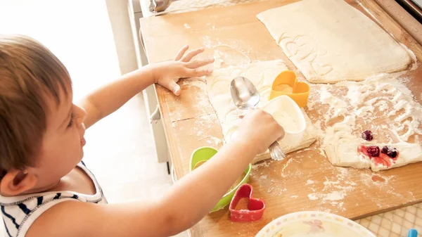Primo piano ritratto di adorabile bambino di 3 anni ragazzo rotolamento pasta di grano con mattarello e biscotti di taglio con speciale figurato taglierina di plastica. Chuld cottura e cottura in cucina — Foto Stock