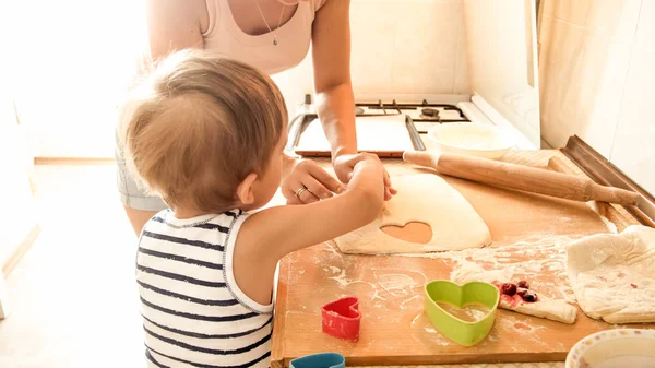 Portret van jonge mooie vrouw onderwijzen haar kleine kind jongen het maken van koekjes en bakken taarten op keuken thuis — Stockfoto