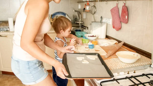 Nahaufnahme Porträt einer jungen Mutter, die ihrem kleinen Sohn das Plätzchenbacken beibringt. Kind mit Eltern backt Desserts auf Backform in Küche im Haus — Stockfoto