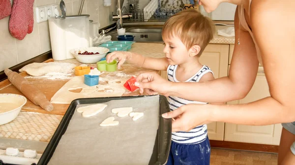 Ritratto ravvicinato di giovane madre con bambino che tiene in mano la teglia e fa biscotti in cucina — Foto Stock