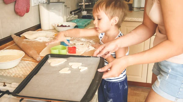 Portret van schattige kleine jongen met jonge moeder bakken koekjes op bakpan in keuken — Stockfoto