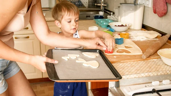 年轻母亲与蹒跚学步的男孩拿着烤盘和在厨房做饼干的特写肖像 — 图库照片