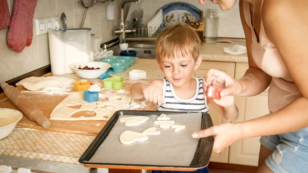 Κοντινό πορτρέτο της νεαρής μητέρας που διδάσκει το νήπιο γιο της φτιάχνοντας μπισκότα. Παιδί με γονείς που μαγειρέψαν επιδόρπια σε ταψί στην κουζίνα στο σπίτι — Φωτογραφία Αρχείου