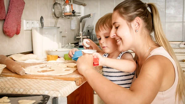 Primo piano ritratto di adorabile bambino di 3 anni che fa biscotti con la madre. CHild tenendo teglia e mettendo i biscotti su di esso — Foto Stock