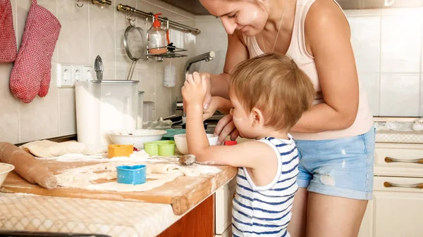 Nahaufnahme Porträt einer jungen Mutter, die ihrem kleinen Sohn das Plätzchenbacken beibringt. Kind mit Eltern backt Desserts auf Backform in Küche im Haus — Stockfoto
