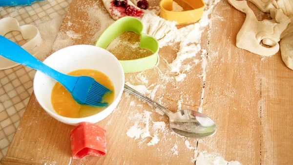Närbild utsikt från hög vinkel på trä skrivbord täckt med mjöl, deg, matlagningsverktyg och ingredienser för matlagning och bakning i köket — Stockfoto
