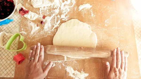 Крупним планом зображення молодої жінки, що прокатує тісто з дерев'яним штифтом. Домогосподарка робить піцу вдома на кухні — стокове фото