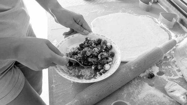 Черно-белый образ молодой женщины, смешивающей ягоды с сахаром в миске во время выпечки сладкого пирога или торта — стоковое фото
