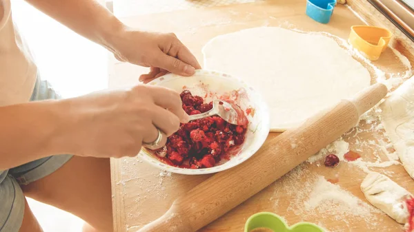 Imagen de primer plano de la joven ama de casa vertiendo azúcar en un tazón grande con bayas fruncidas mientras hace salsa para pastel — Foto de Stock
