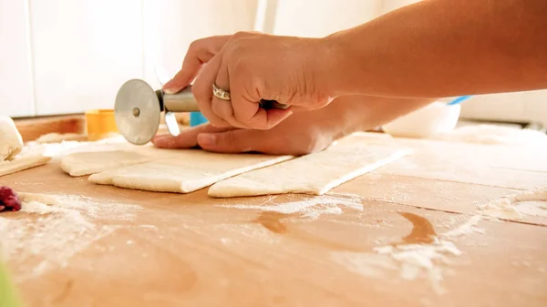 Closeup image of female hand holding round knife for pizza and cutting dough on big wooden desk on kitchen — Stock Photo, Image