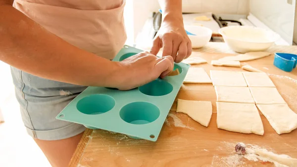 Closeup image of young woman picking up piece of dough and putting it in silicone form for baking in oven. Housewife making cupcakes at home — Stock Photo, Image