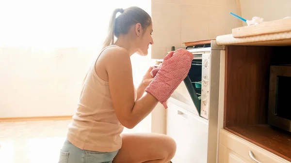 Getöntes Foto von schönen lächelnden Hausfrau setzen Backform mit rohen Plätzchen in heißen Ofen in der Küche — Stockfoto