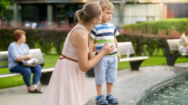 Portrait of young mother caressing and calming her crying toddler son in park. — Stock Photo, Image